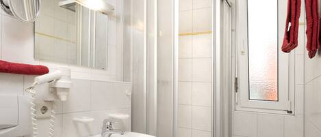 A bathroom with a white sink, a mirror, a hairdryer, and a shower enclosure.