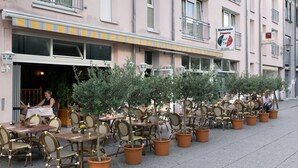 Un edificio con una fila de mesas y sillas al aire libre, un letrero de restaurante y una persona sentada en una mesa.