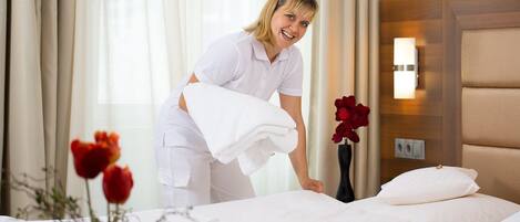 A hotel room with a neatly made bed, a vase with red flowers, and a wooden headboard.