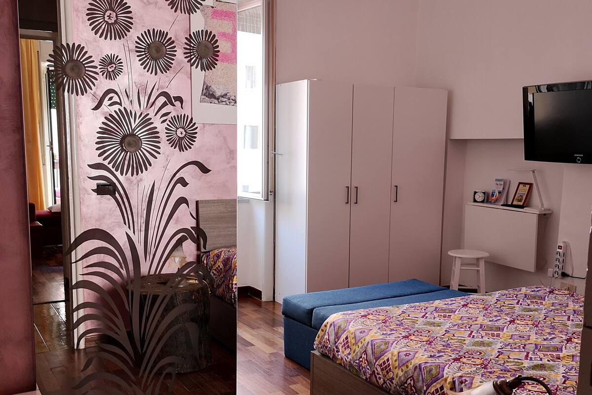 A bedroom with a bed, a dresser, a vanity, and a TV.