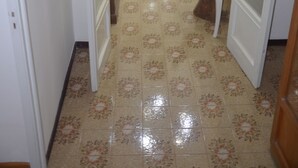 A hallway with a patterned floor, a wooden bench, and a table with a bottle and a vase. - Smiling Naples (Naples)