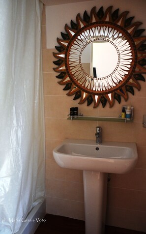 A bathroom with a sunburst mirror, a pedestal sink, and a shower curtain. - Smiling Naples (Naples)
