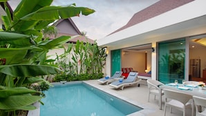 A modern outdoor pool area with lounge chairs and a dining table, surrounded by lush greenery. - Villa Karina (Rawai)