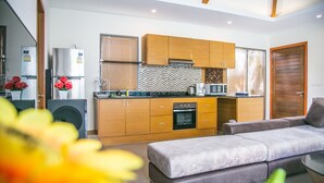 A modern kitchen with wooden cabinets, a built-in oven, and a dining area with a grey sofa. - Villa Karina (Rawai)