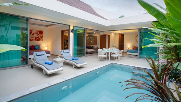 A modern pool area with lounge chairs, a dining table, and a glass-enclosed bedroom. - Villa Karina (Rawai)