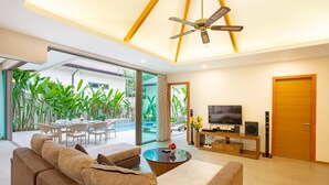 A modern living room with a sofa, coffee table, TV, and a ceiling fan. - Villa Karina (Rawai)