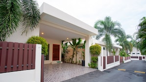 A modern building with a covered entrance, a gated driveway, and lush greenery. - Villa Karina (Rawai)