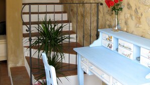A staircase with a stone wall, a white chair, a table with drawers, and a vase with red flowers. - Country Club Da Cesco (Borso del Grappa)