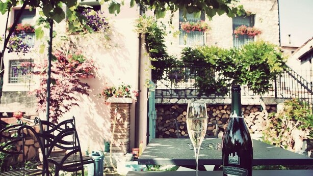 A table with a bottle of wine and a glass of wine, set outdoors with a view of a stone building and greenery. - Country Club Da Cesco (Borso del Grappa)
