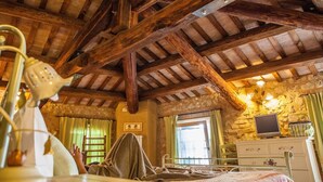 A rustic room with exposed wooden beams, a bed, a dresser, and a television on a stone wall. - Country Club Da Cesco (Borso del Grappa)