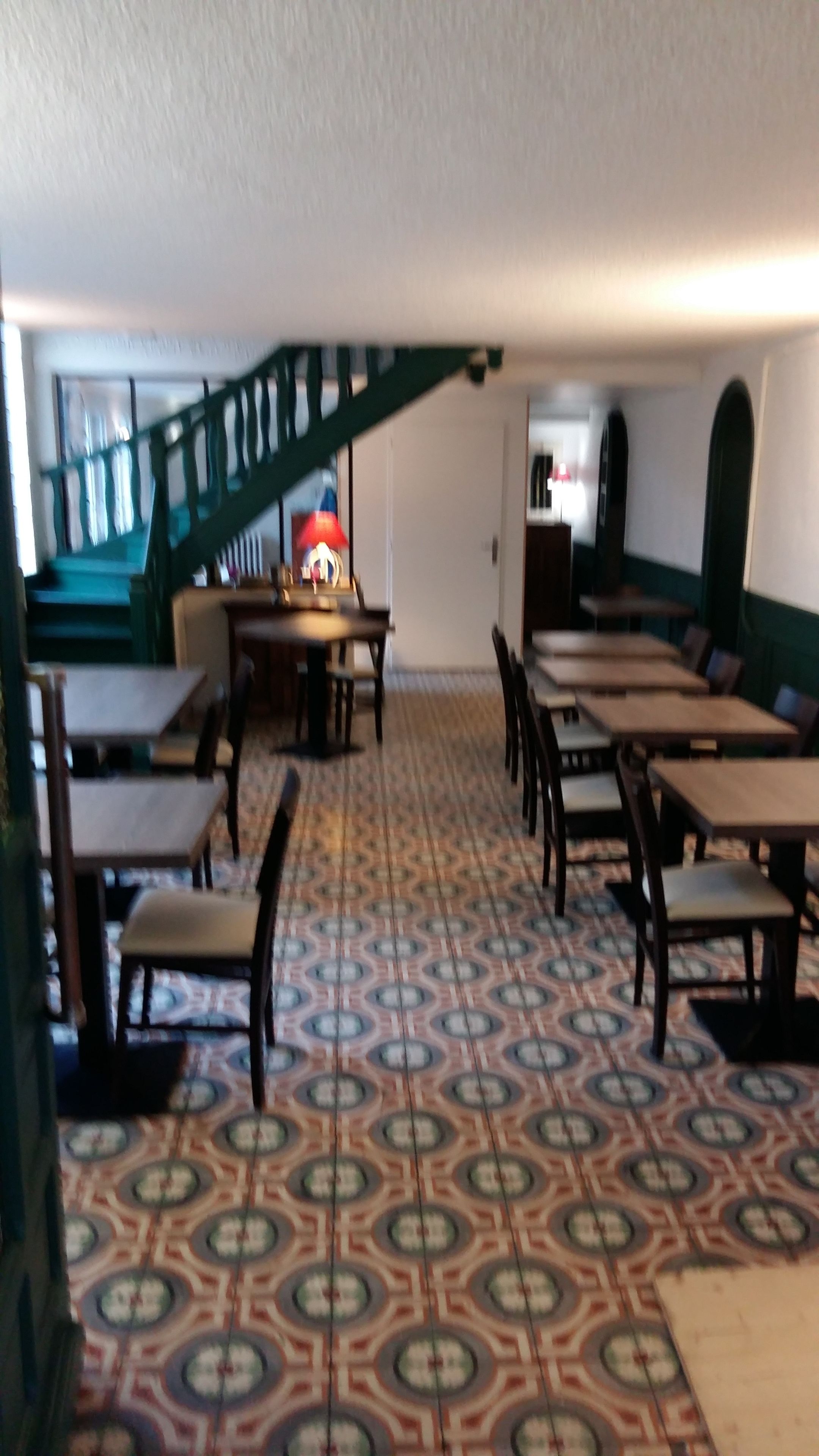 Un comedor con piso estampado, mesas y sillas de madera, y una escalera que sube a otro nivel.