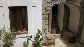 Un arco in pietra che conduce a un'area piccola e recintata con una finestra e piante in vaso.
