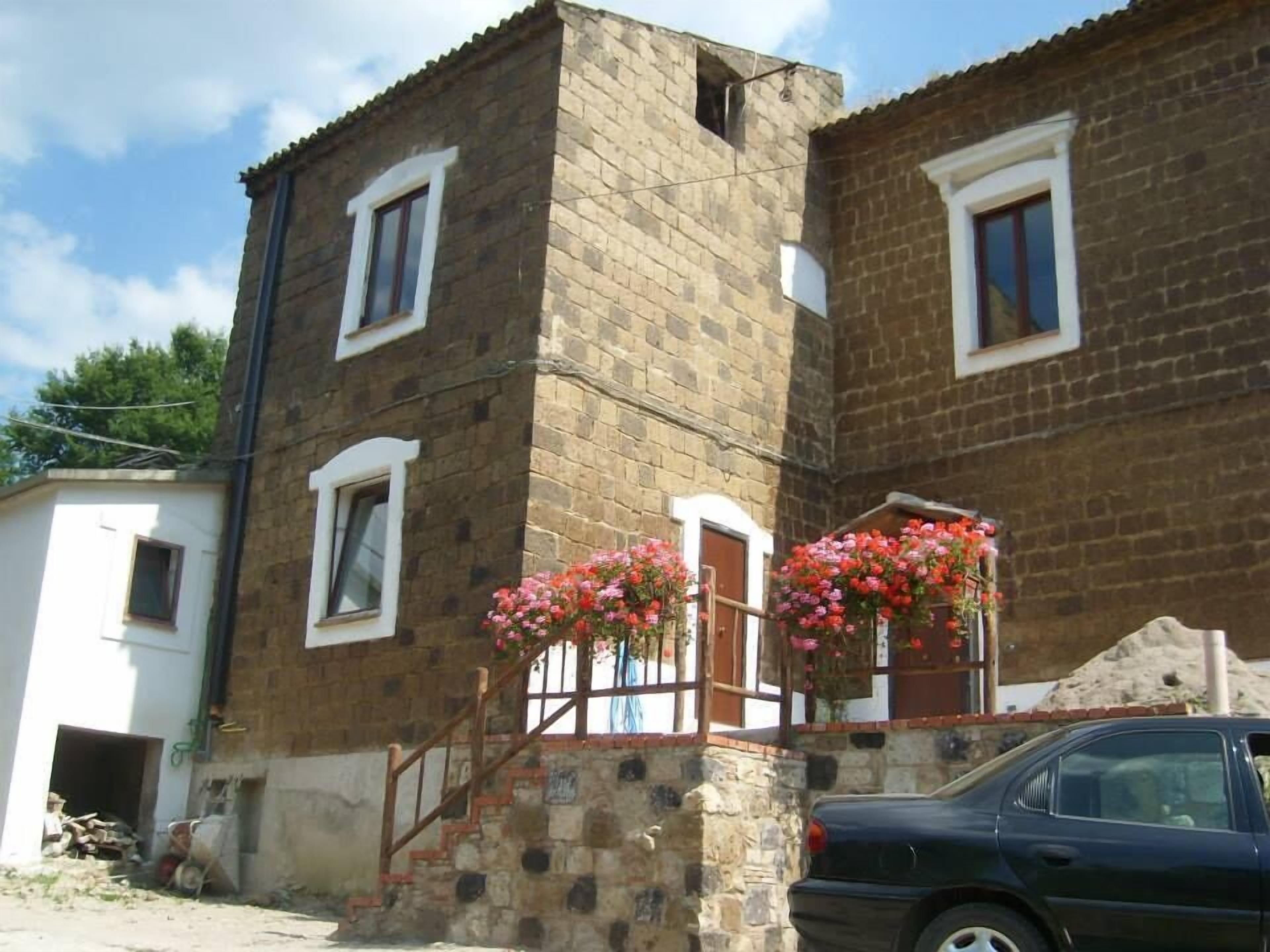 Un edificio a due piani con facciata in pietra, una scala in legno e un'auto parcheggiata davanti.