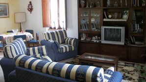 Ein Wohnzimmer mit einer Sofagarnitur, einem Fernseher und einem Holzschrank mit Glastüren.