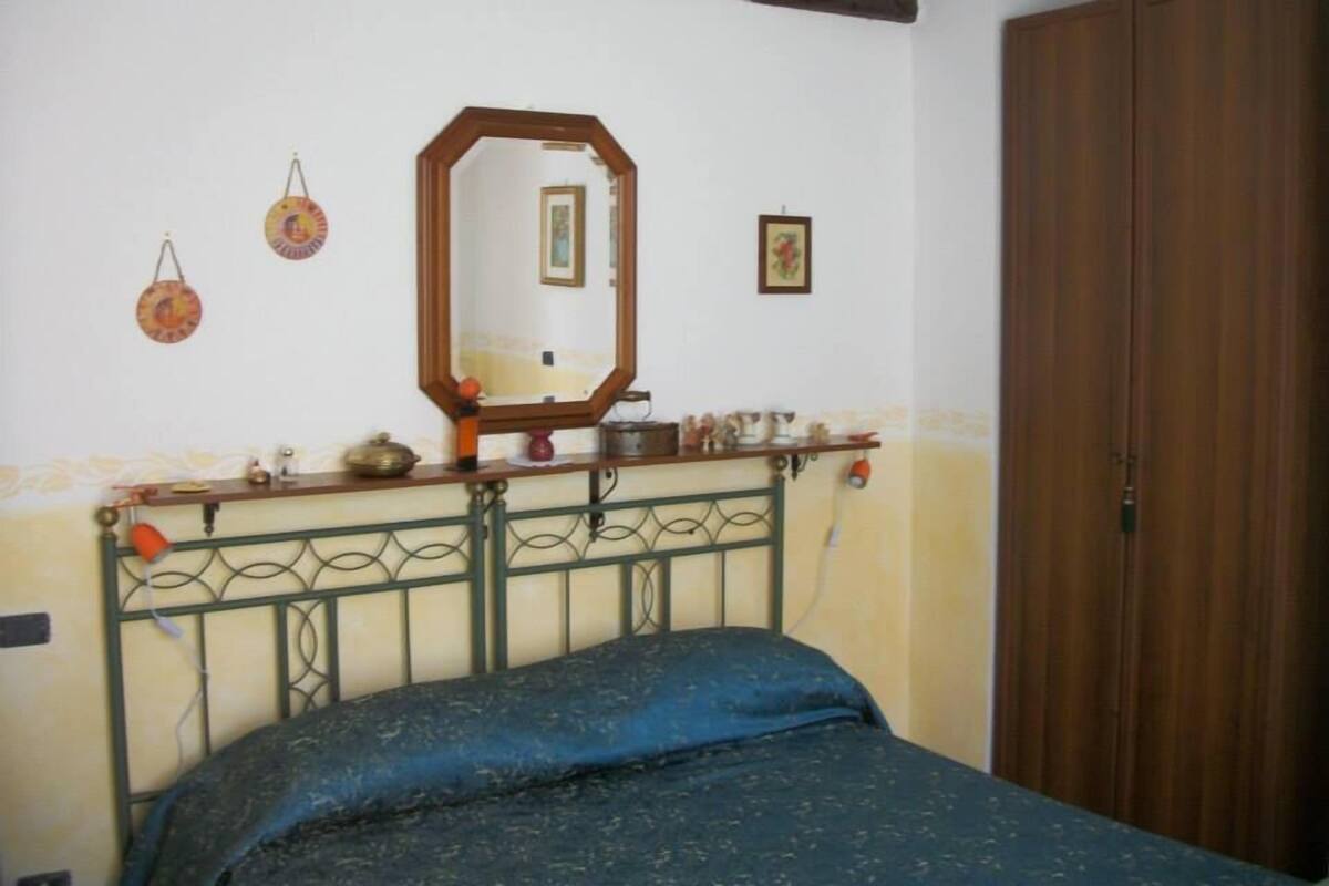 Un dormitorio con cama, un armario de madera, un espejo y una estantería con diversos objetos.