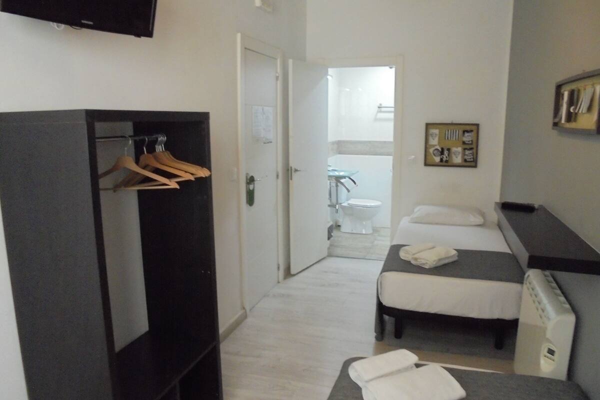 A hotel room with a wardrobe, two beds, a TV, and a bathroom visible through an open door.
