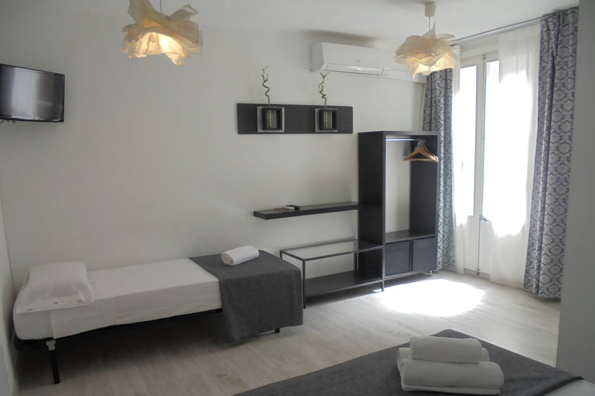 A modern bedroom with a bed, a TV, a shelf, and a hanging light fixture.