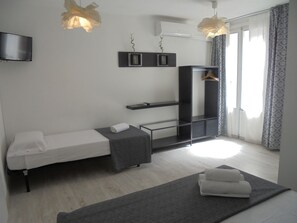 A modern bedroom with a bed, a TV, a shelf, and a hanging light fixture. - Easy Sants by Bossh Hotels (Barcelona)