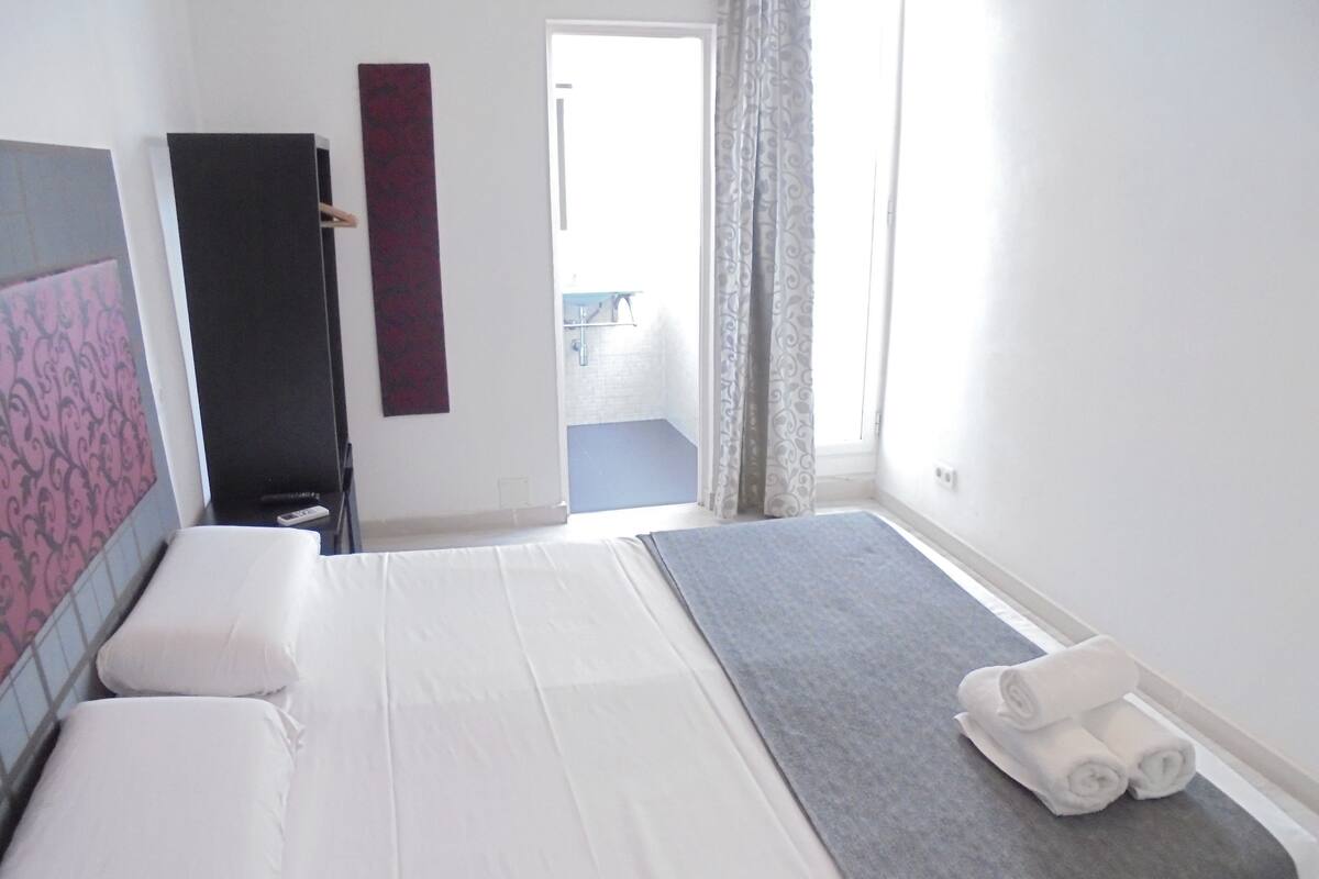 A bedroom with a bed, a bedside table, a towel rack, and a view of a balcony.