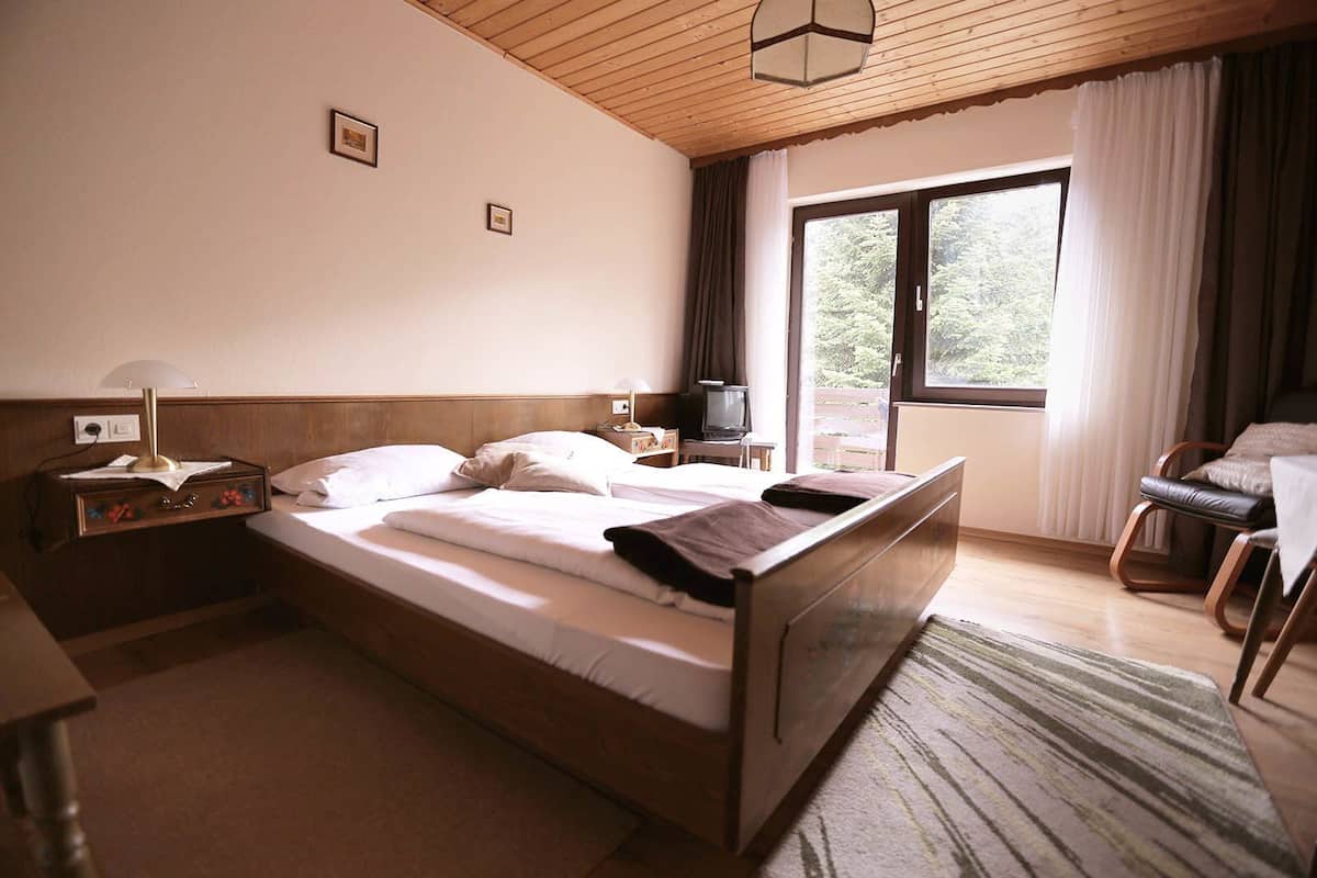 Habitación de hotel con una cama de madera, un escritorio con lámpara, televisor y vistas al exterior.