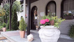 A building entrance with a stone statue, potted plants, and a large planter with flowers. - Hotel Rennsteig (Steinbach am Wald)