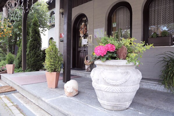 Entrada de um edifício com uma estátua de pedra, plantas em vasos e um vaso grande com flores.