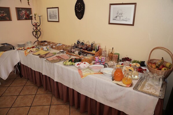 A buffet table with various food items and beverages, framed pictures on the wall, and a clock.
