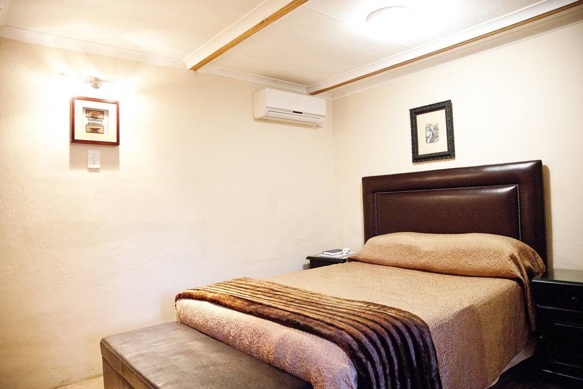 Makuuhuoneessa on sänky, yöpöytä, seinälle asennettu ilmastointilaite ja seinällä oleva kehystetty taulu.
