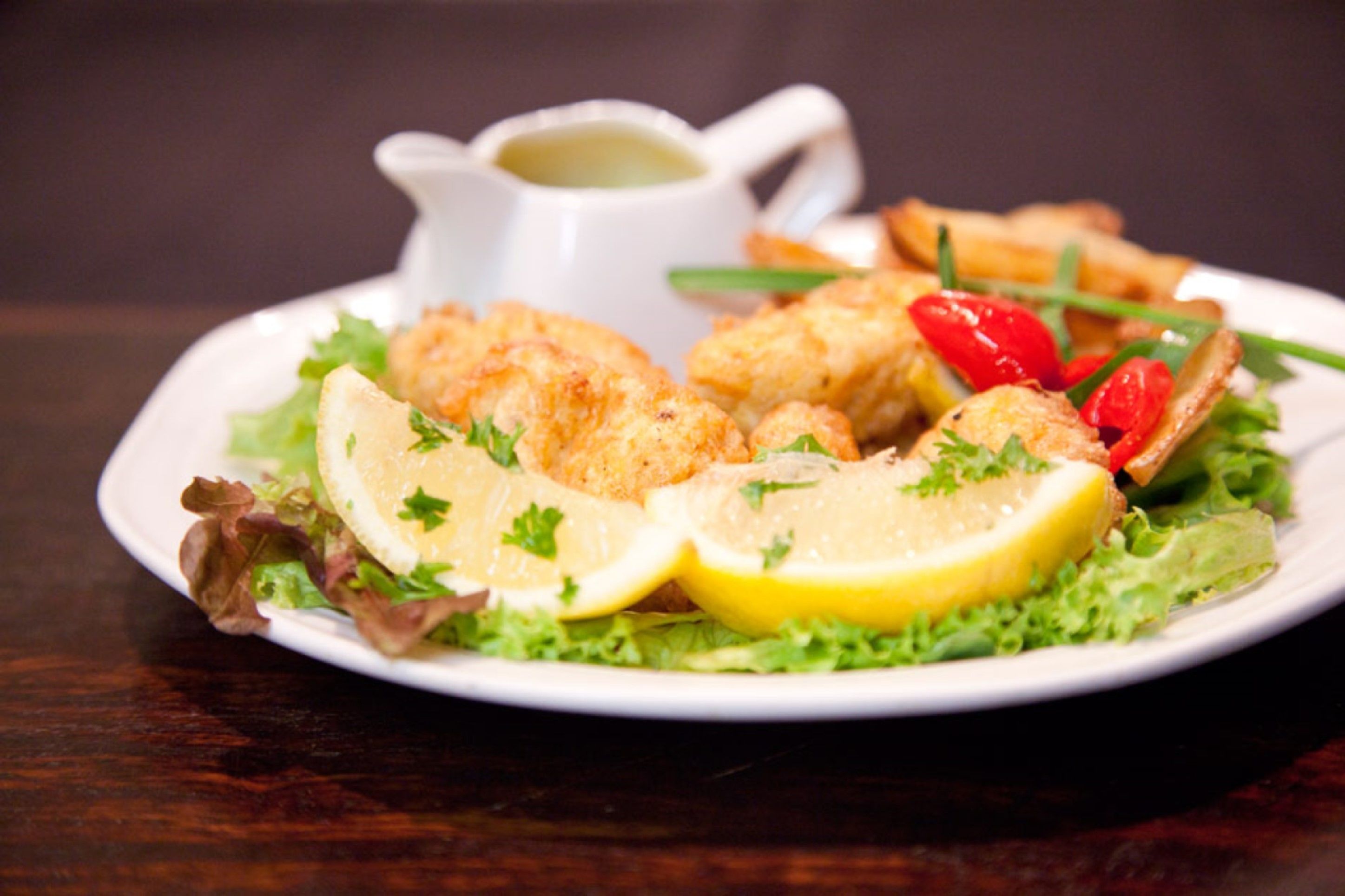 A plate of food with lemon slices, greens, and a small cup of sauce.