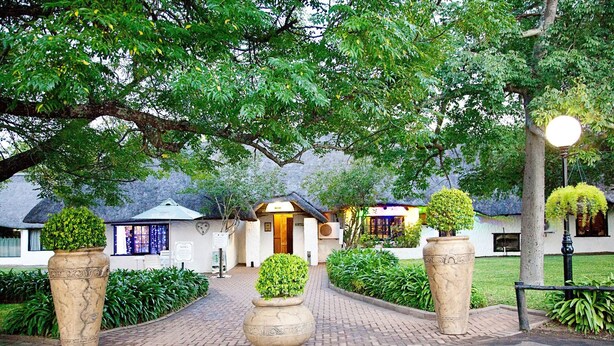 A pathway leading to a building with a thatched roof, surrounded by greenery and large planters. - Lalapanzi Hotel and Conference Centre (Louis Trichardt)