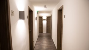 Un couloir étroit et bien éclairé, avec des portes en bois et un mur blanc et immaculé.