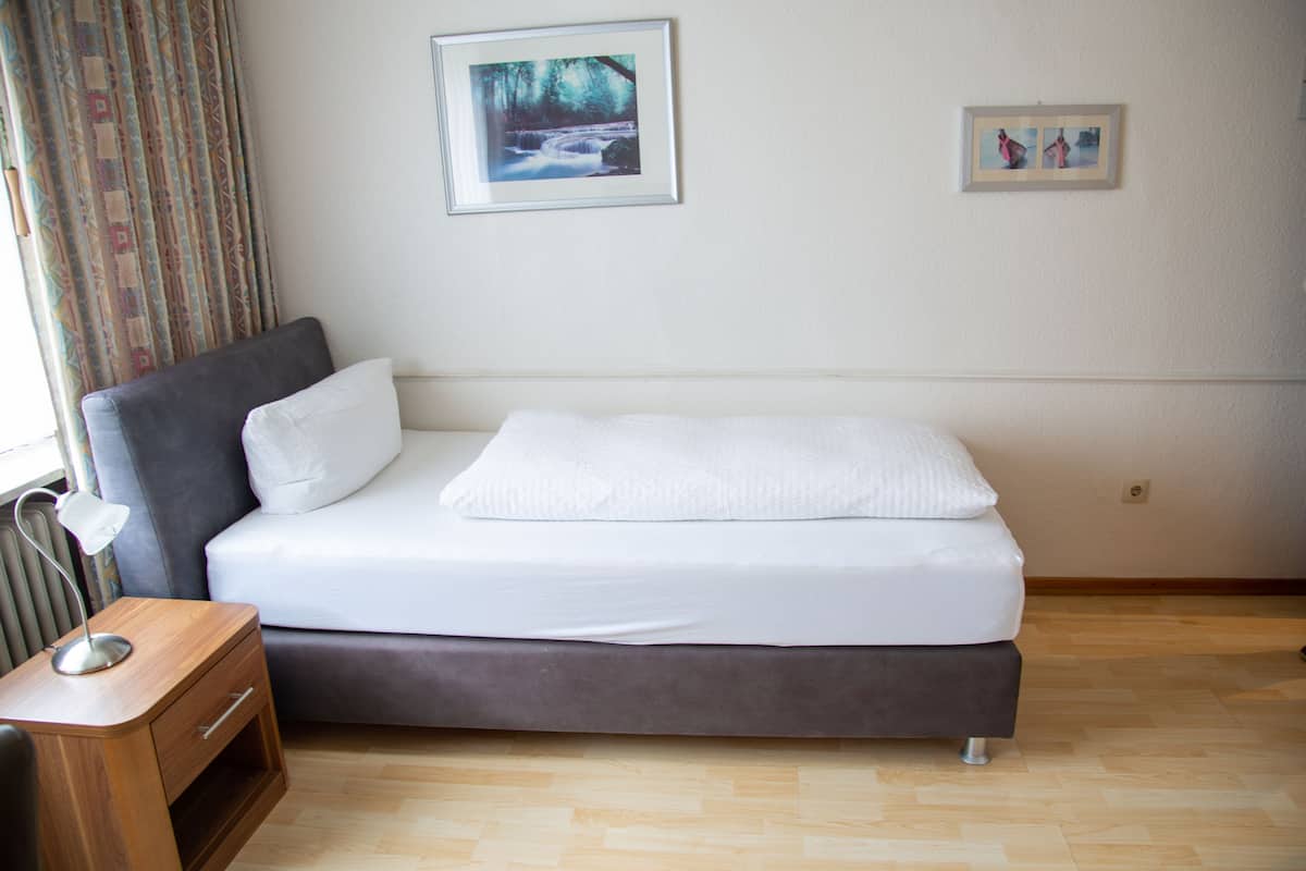 Un dormitorio moderno con un sofá cama gris, una mesita de noche de madera con una lámpara, y dos cuadros enmarcados en la pared.