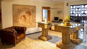Une pièce spacieuse, ornée d’un grand tableau, d’un canapé en cuir, d’une table à plateau de verre et d’une colonne en pierre.