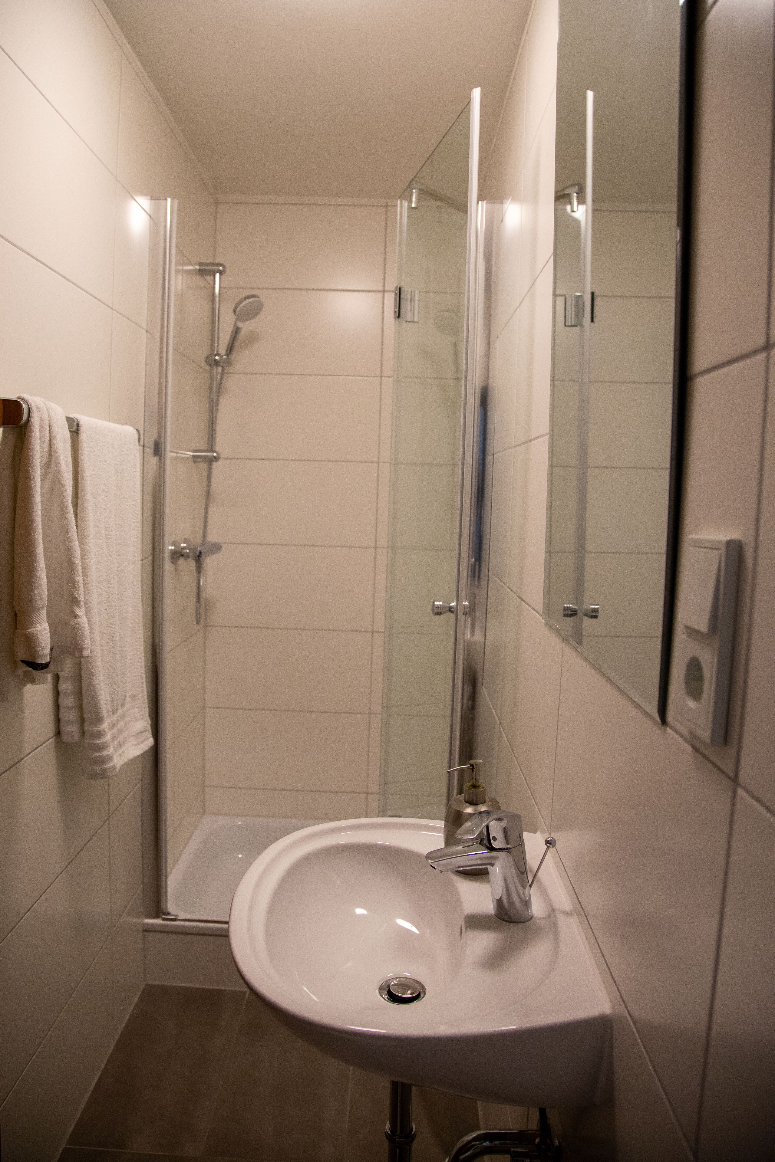 A modern bathroom with a glass-enclosed shower, a white sink, and a mirror.
