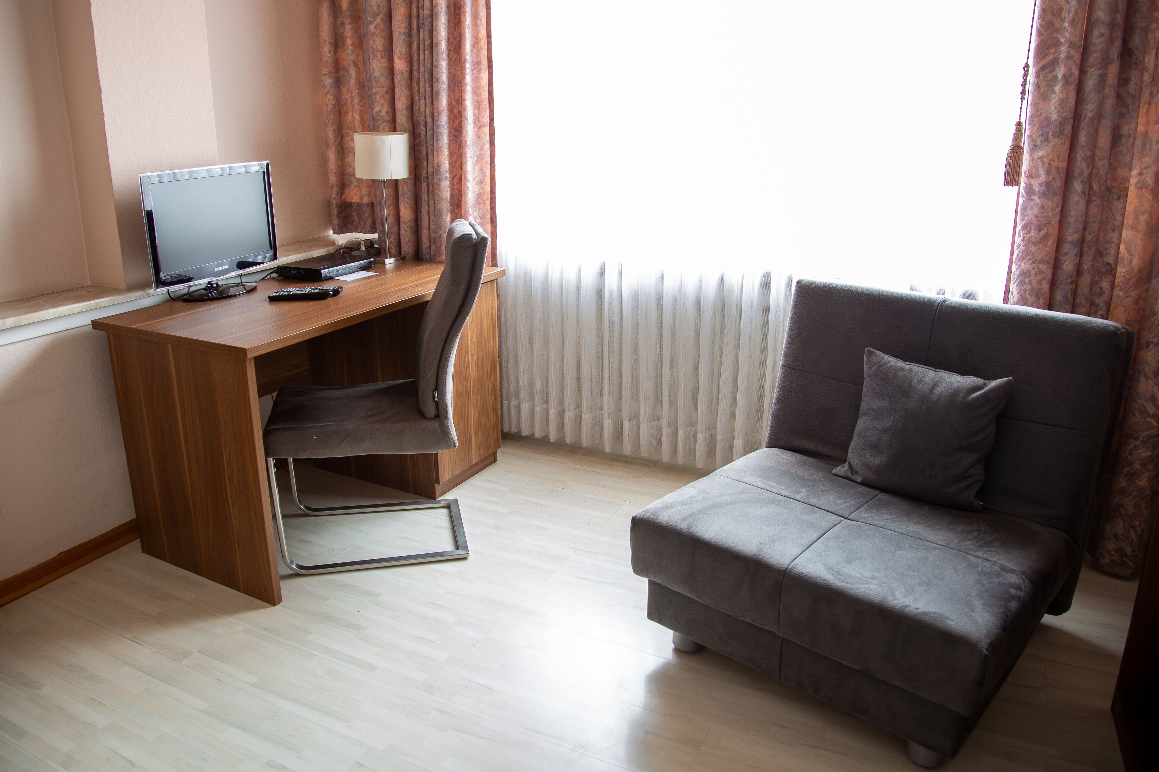 A modern room with a wooden desk, a grey sofa, and a large window with curtains.