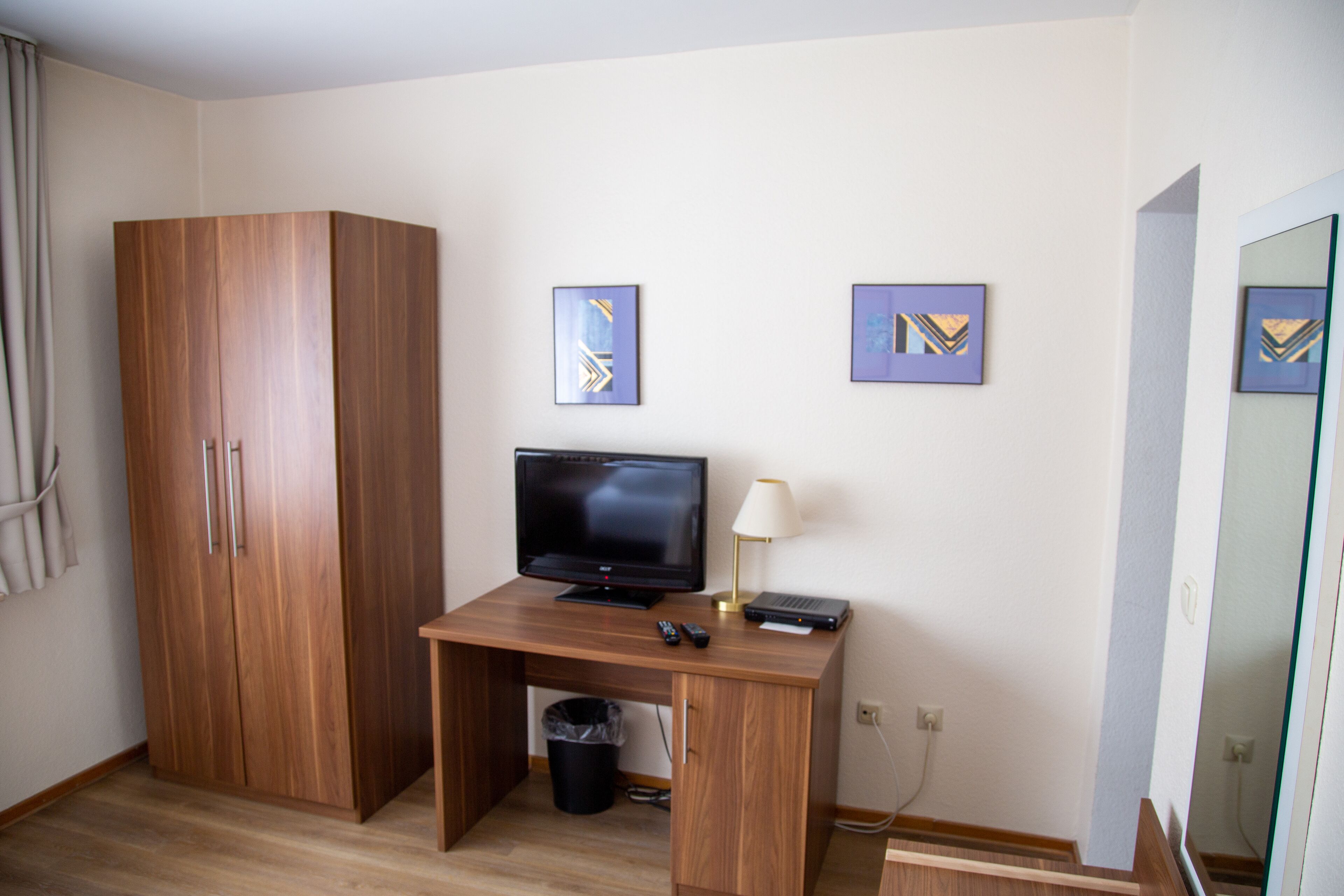 Una habitación de hotel con un escritorio de madera, un televisor, una lámpara y dos obras de arte enmarcadas en la pared.