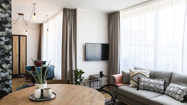 A modern living room with a round wooden table, grey sofa, and a flat-screen TV. - rent24 Apartments & Suiten P180 (Berlin)