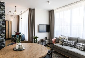 Un salon moderne avec une table ronde en bois, un canapé gris et un téléviseur à écran plat.