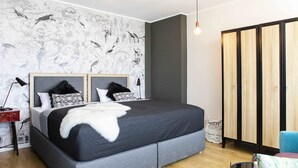 A modern bedroom with a large bed, a wardrobe, and a wall with a bird and floral wallpaper. - rent24 Apartments & Suiten P180 (Berlin)