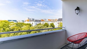A balcony with a red chair, a wall-mounted light fixture, and a view of buildings and trees. - rent24 Apartments & Suiten P180 (Berlin)