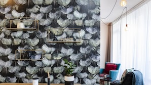 A modern living room with a black and white leaf-patterned wallpaper, a wooden reception desk, a potted plant, and a blue armchair. - rent24 Apartments & Suiten P180 (Berlin)
