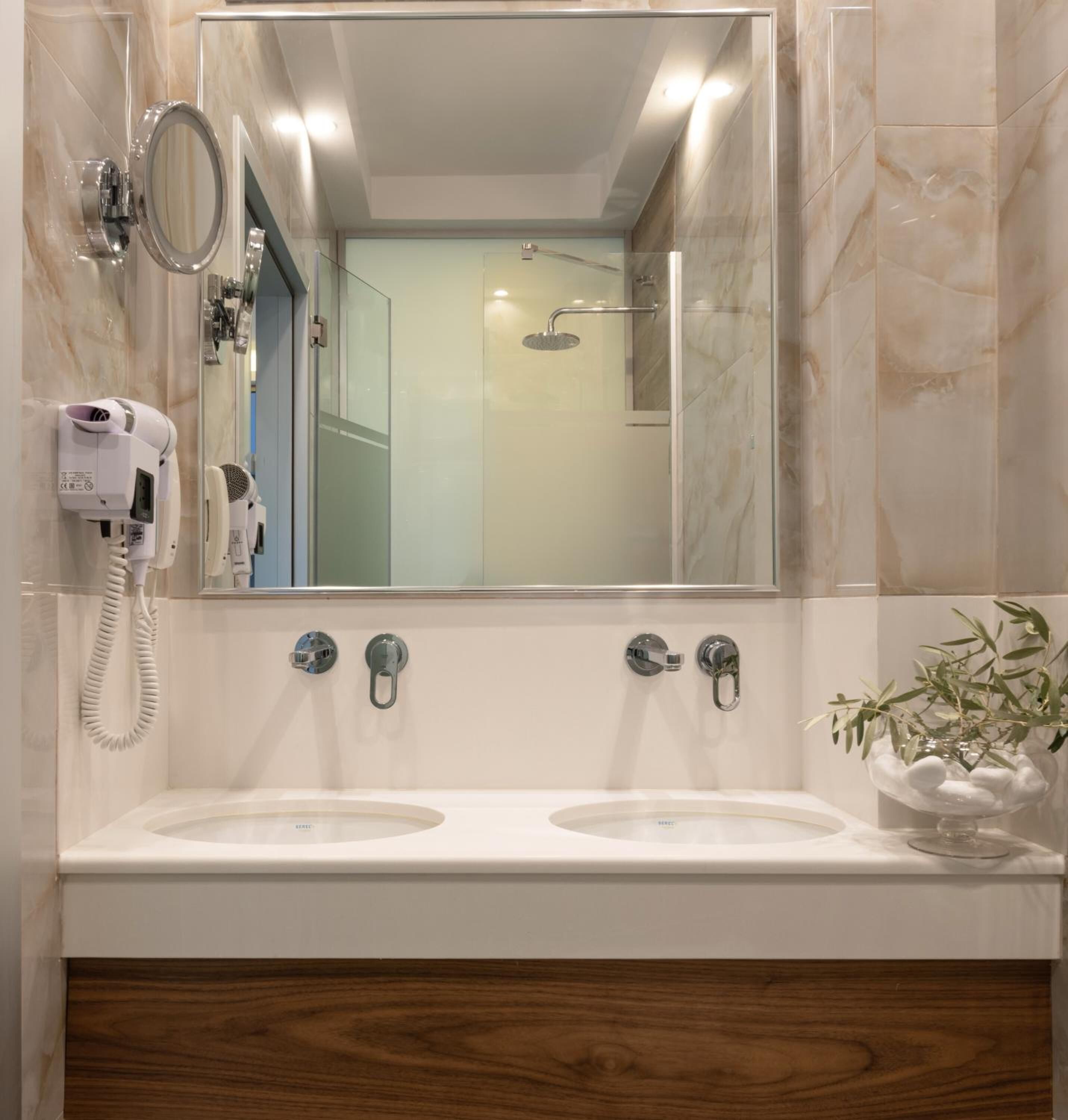 Un baño con un espejo grande, dos lavamanos, un secador de pelo y una ducha.