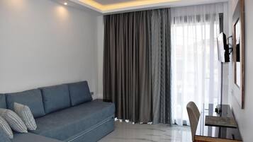 A modern living room with a grey sofa, a wooden side table, and a large window with sheer curtains.