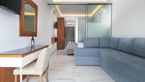 A modern living room with a grey sectional sofa, a wooden desk with a chair, a television mounted on the wall, and a glass door leading to another room. - 4-You (Polygyros)