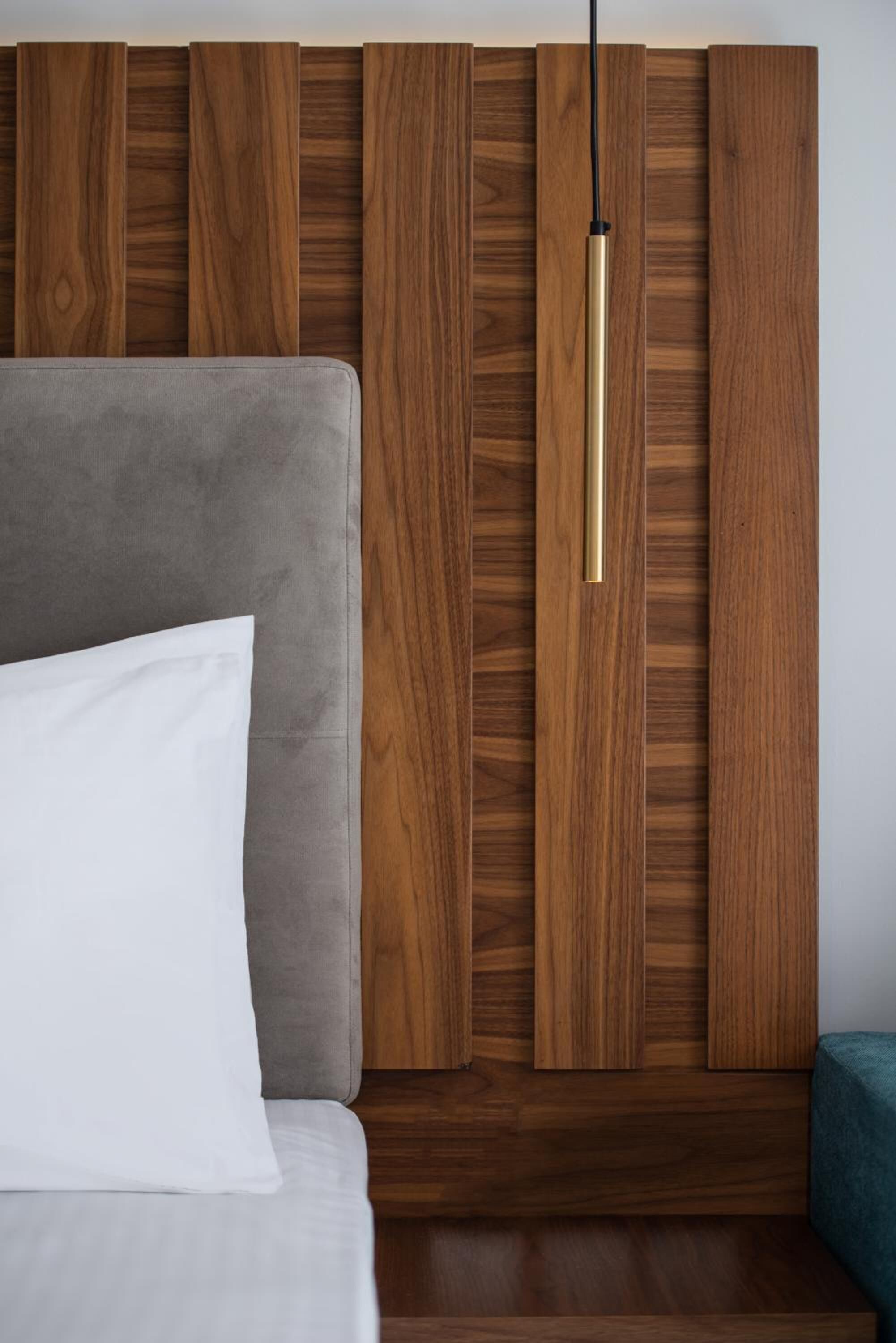 Une chambre à coucher avec une tête de lit rembourrée de couleur grise, un oreiller blanc et un mur recouvert de panneaux en bois, agrémenté d’une suspension lumineuse.
