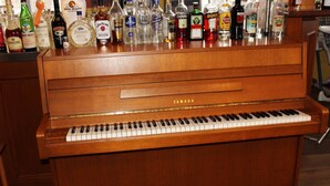 A Yamaha upright piano with a variety of liquor bottles on top. - Deutsches Haus (Waal)