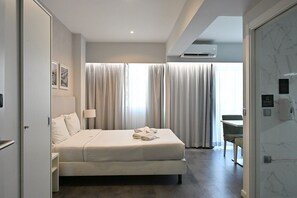 A modern hotel room with a bed, a desk, and a view of the outside through large curtains. - My Charm Lisbon Suites (Lisbon)