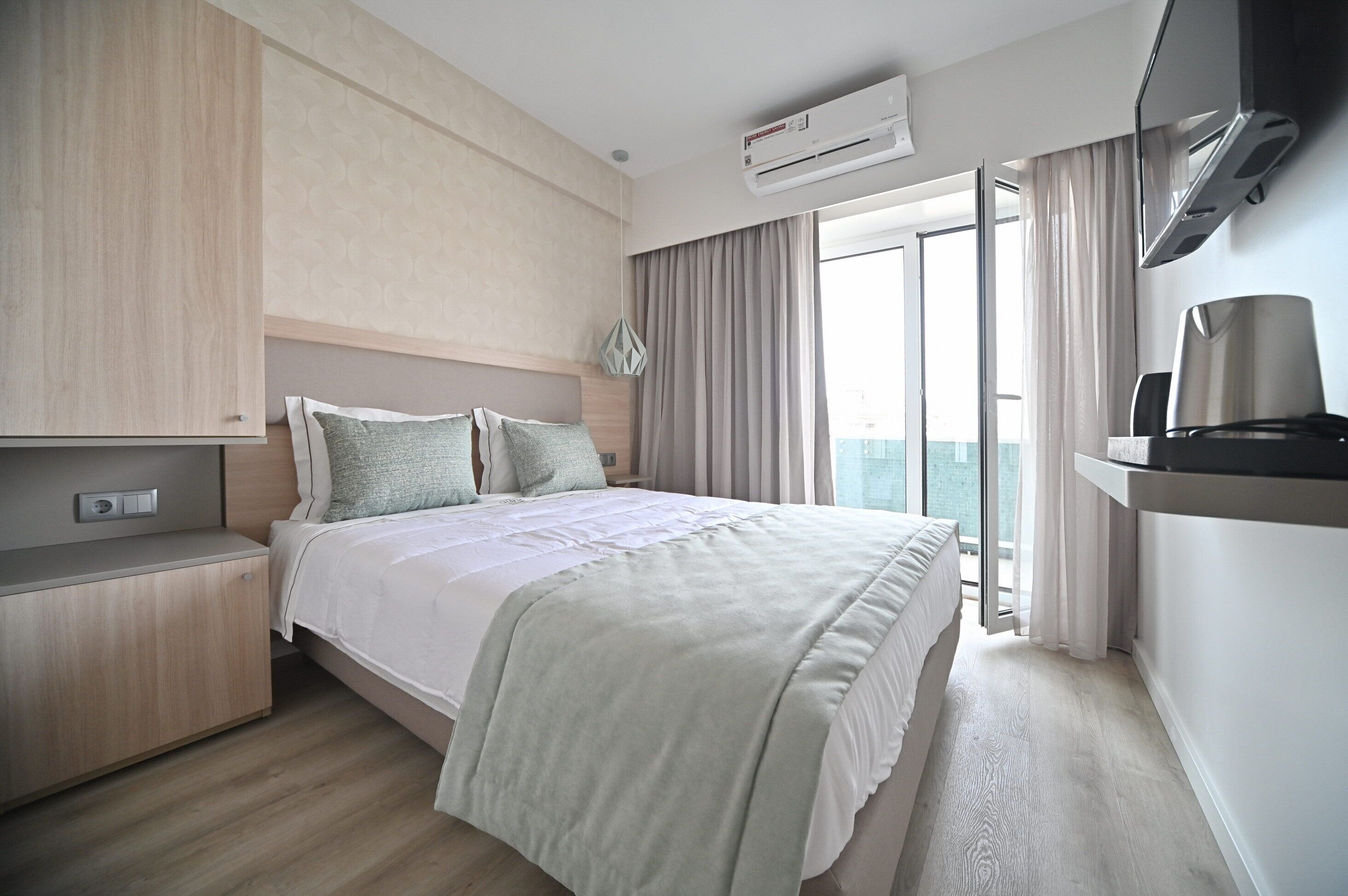 A modern hotel room with a large bed, a wooden nightstand, a flat-screen TV, and a balcony with curtains.