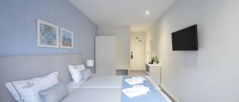 A hotel room with two beds, a flat-screen TV mounted on the wall, and a bathroom visible in the background.