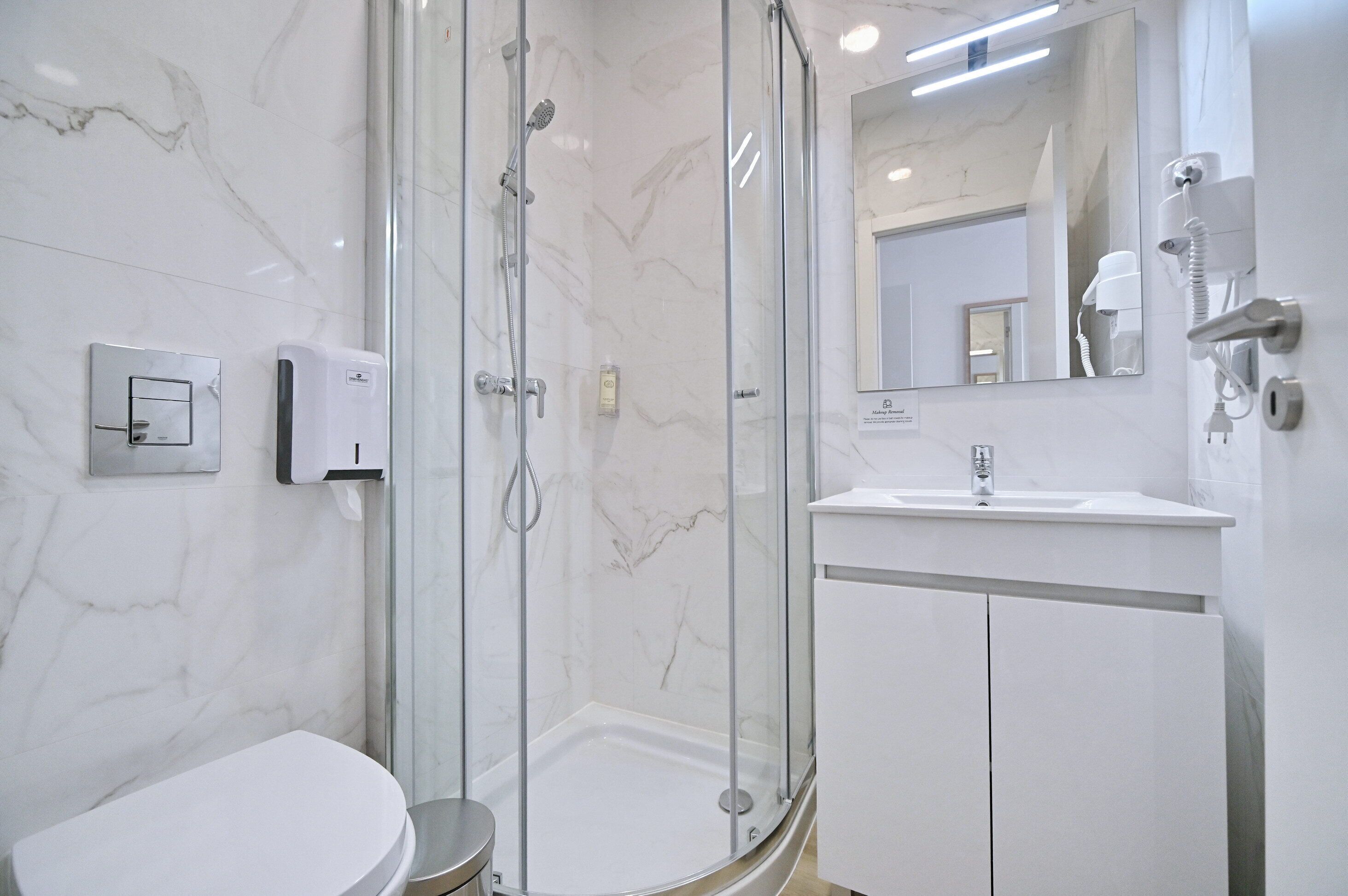 Un baño moderno con ducha de vidrio, lavamanos blanco y pared con azulejos de mármol.
